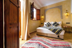 A bedroom with a bed, a wooden door, a window, a wall-mounted light fixture, and a patterned rug. - Riad Chalymar (Marrakech)