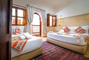 Habitación de hotel con dos camas, un tapete estampado y vistas a través de una puerta abierta.