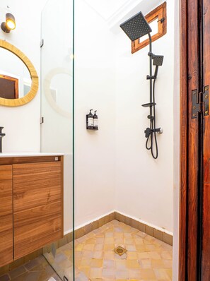 A bathroom with a wooden vanity, a glass shower enclosure, and a tiled floor.