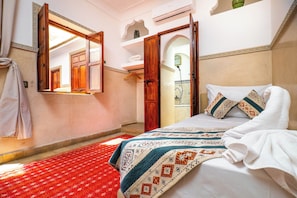 Un dormitorio con cama, un espejo grande, un armario y un baño visible a través de una puerta abierta.
