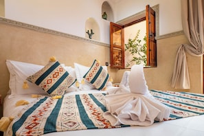 Une chambre d’hôtel comprenant un lit, des oreillers, une couverture, une fenêtre avec des rideaux et un élément de décoration fixé au mur.