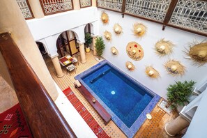 A rooftop pool area with a blue pool, surrounded by decorative sun hats, potted plants, and a seating area with a table and chairs. - Riad Chalymar (Marrakech)