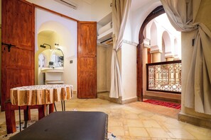 A room with a wooden door, a table, a bench, and a view of an outdoor area with a railing. - Riad Chalymar (Marrakech)