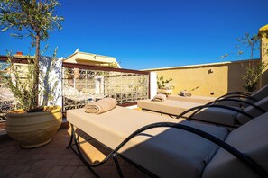 A rooftop terrace with lounge chairs, a decorative metal gate, and potted plants. - Riad Chalymar (Marrakech)
