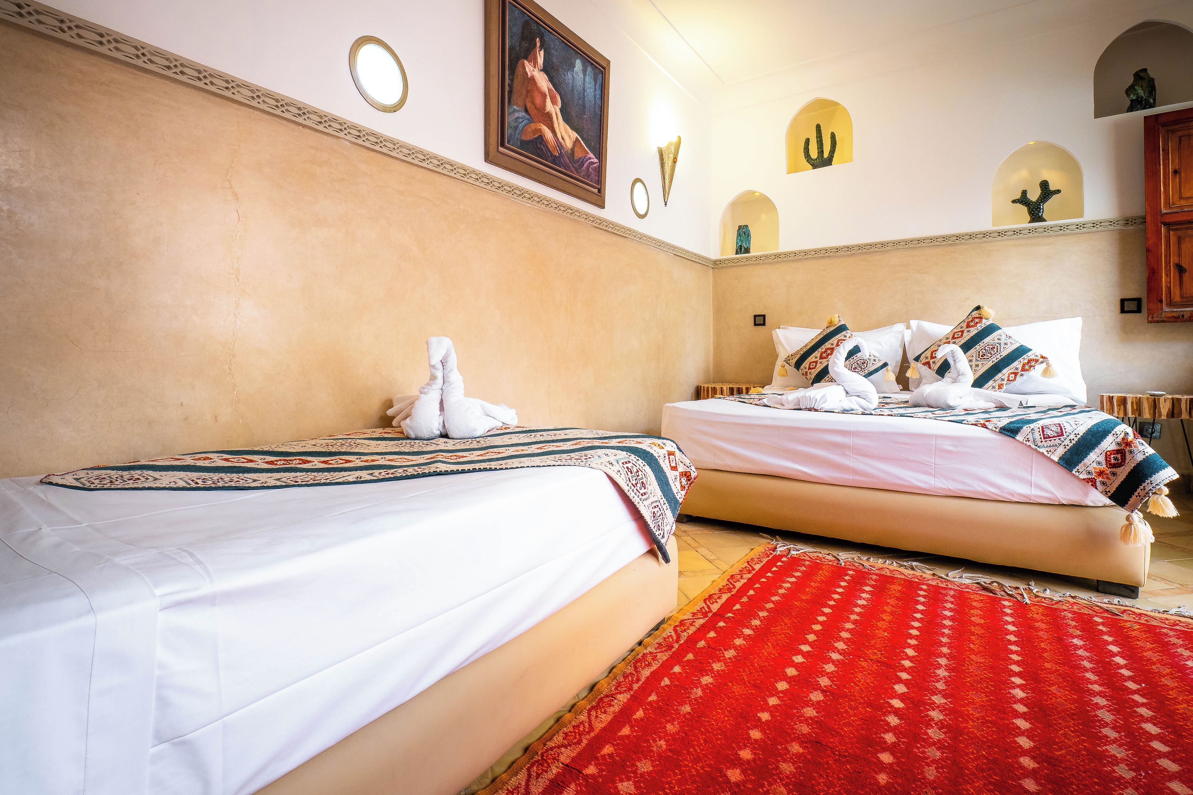 Habitación de hotel con dos camas, un tapete rojo estampado y detalles decorativos en la pared.