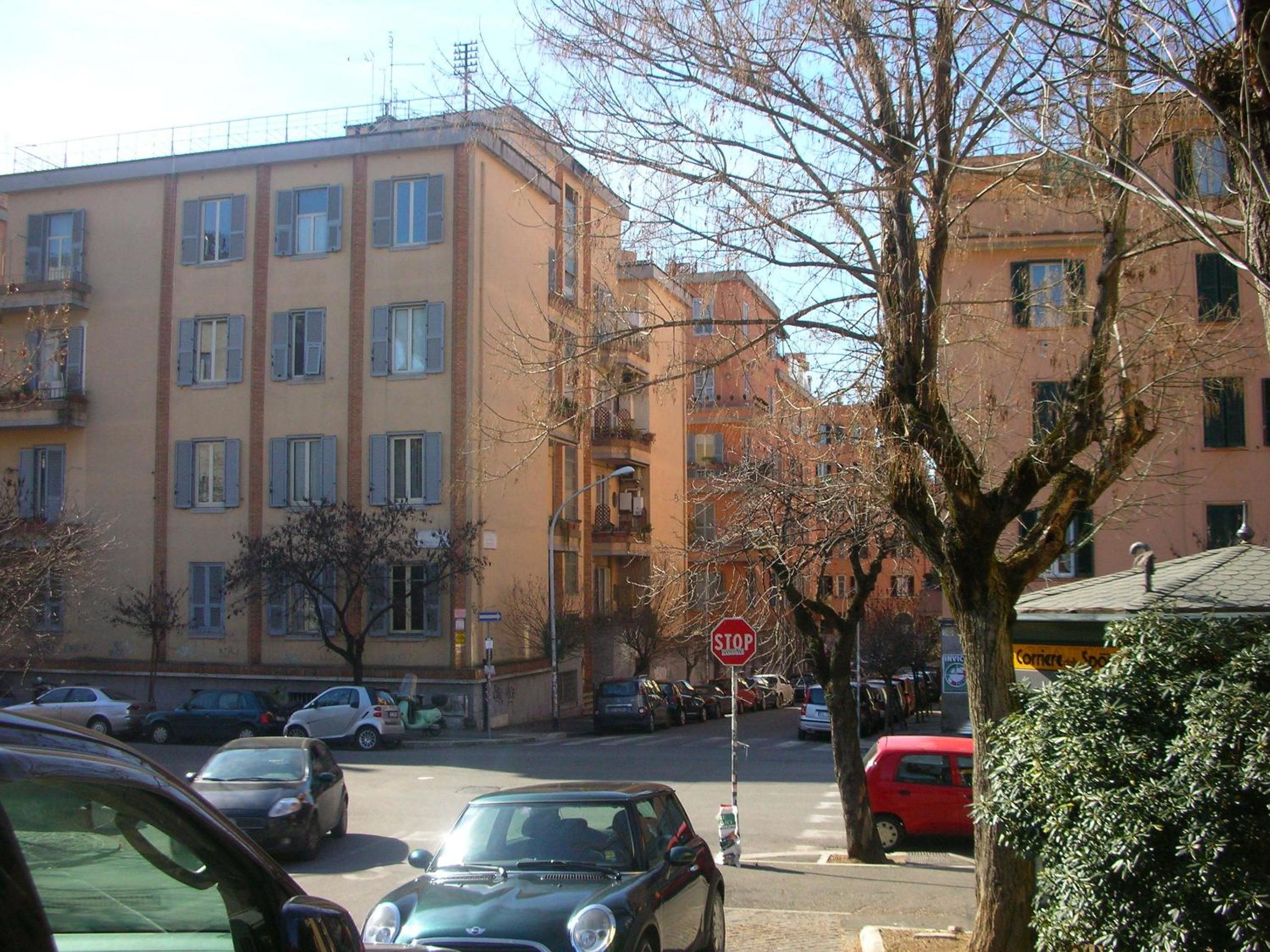 Straßenansicht mit parkenden Autos, einem Stoppschild und mehrstöckigen Gebäuden mit Balkonen.