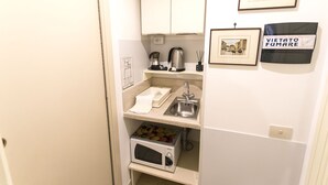 A compact kitchenette with a microwave, kettle, and coffee maker. There are framed pictures on the wall and a sign that reads "VIEITO FUMARE". - A Casa Cibella (Rome)