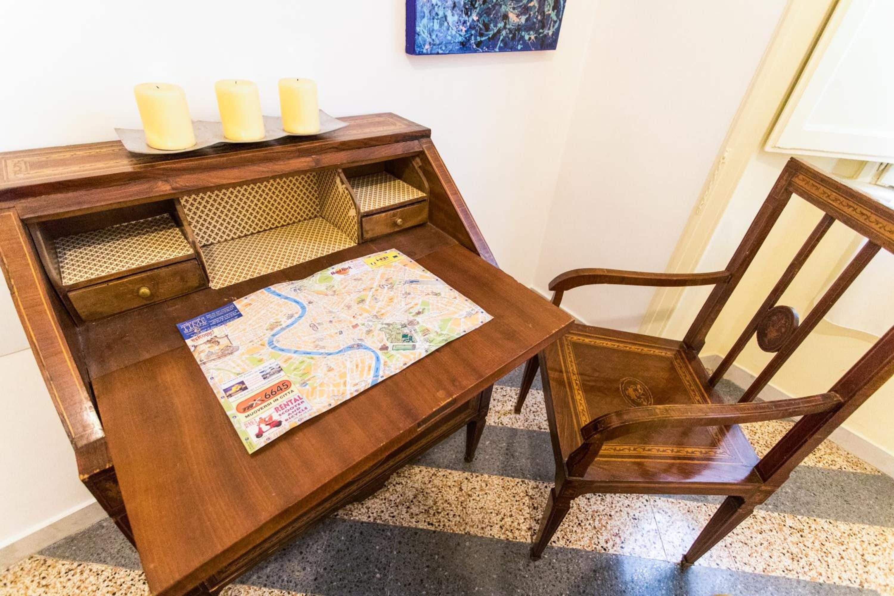 A wooden desk with a map, a chair, and three candles.