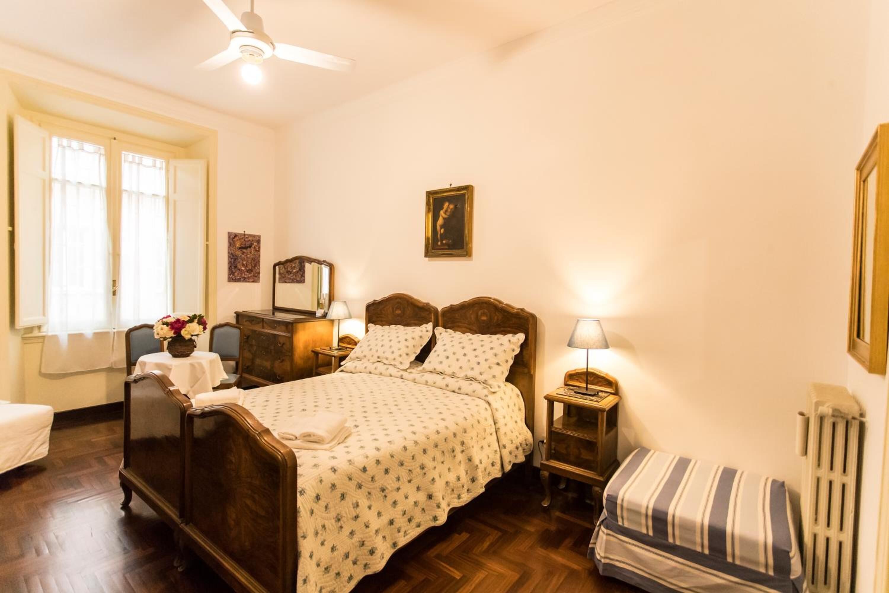 Un dormitorio con cama de madera, mesitas de noche, un radiador y una ventana con cortinas.