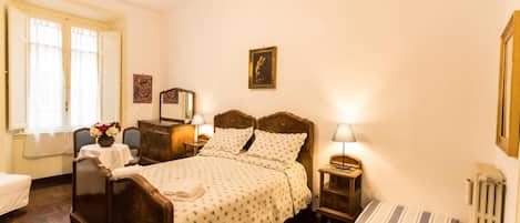 A bedroom with a wooden bed, bedside tables, a radiator, and a window with curtains.