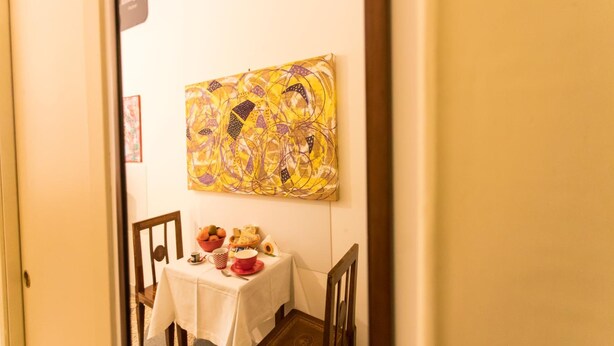 A dining area with a table set for two, a painting on the wall, and a door leading to another room. - A Casa Cibella (Rome)