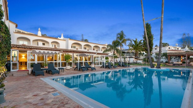 A swimming pool with lounge chairs, a covered seating area, and a building with arched windows and a tiled roof. - Hotel Cerro da Marina (Albufeira)