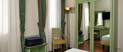 Una habitación de hotel con una cama, una silla, un escritorio, un espejo y cortinas.