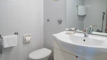 Et badeværelse med et hvidt toilet, en vask med et spejl og en håndklædestang.