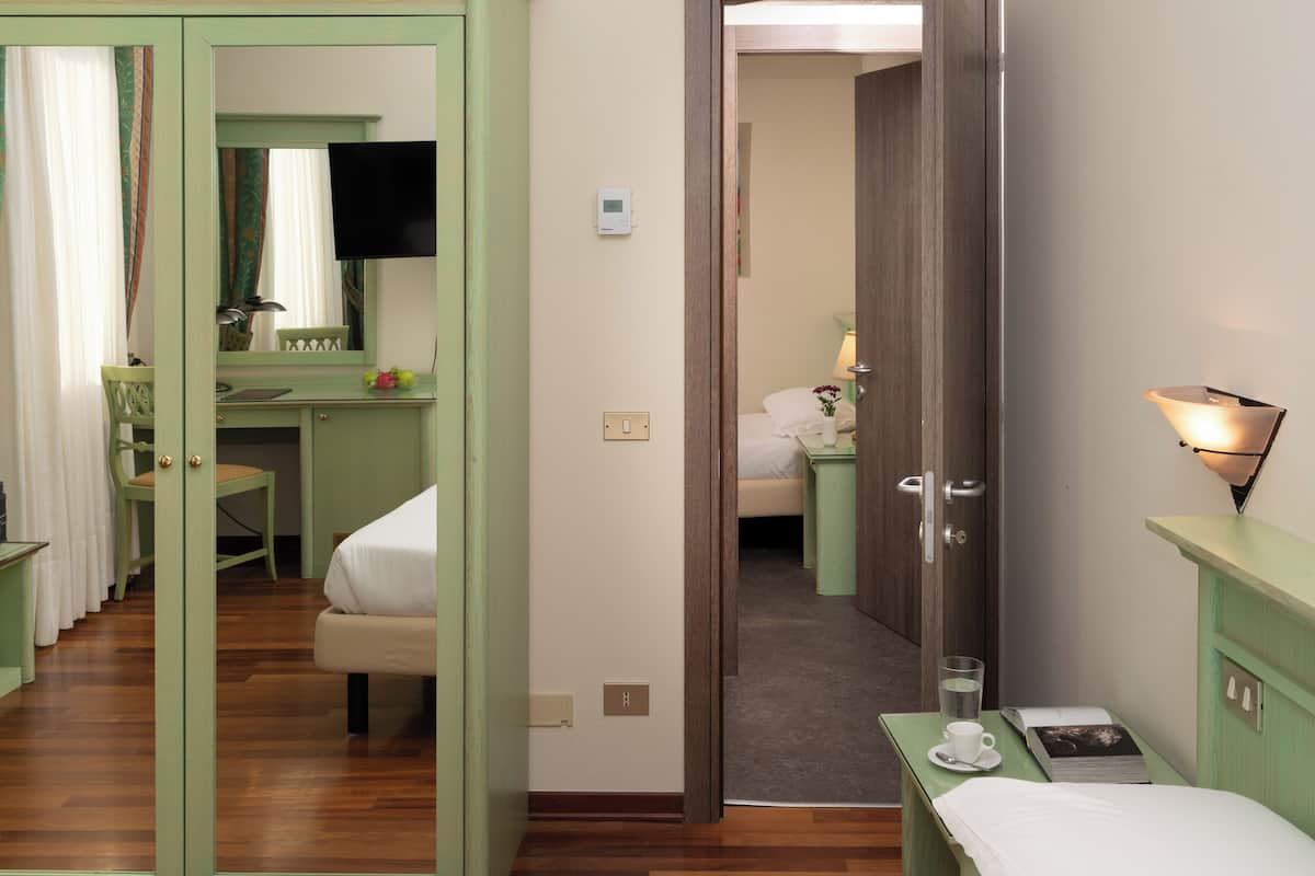 Habitación de hotel con cama, escritorio y silla, televisión y mesita de noche con lámpara.