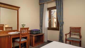 Ein Hotelzimmer mit einem Holztisch, zwei Stühlen, einem Bett, einem Fenster mit Vorhängen und einem Spiegel.