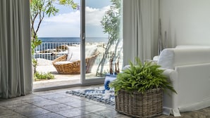 A living room with a white sofa, a wicker basket with green plants, and a view of the sea through a glass door. - Arbatax Park Resort - Suites del Mare by Falkensteiner (Tortoli)