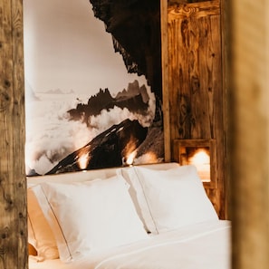 A bedroom with a bed, pillows, a wooden headboard, and a wall with a mountain landscape. - Corona (CORTINA D´AMPEZO)