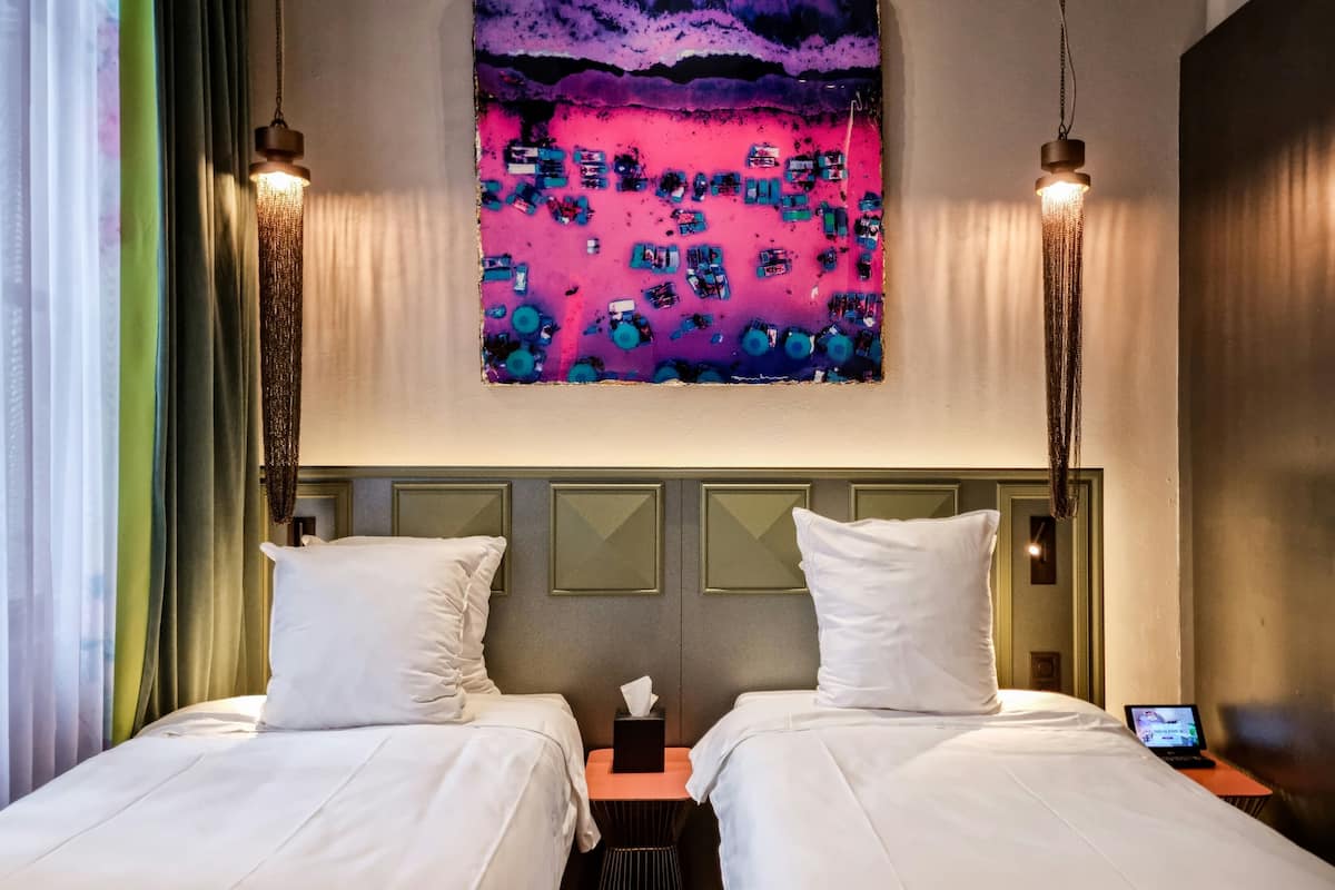 Una habitación de hotel con dos camas, un cuadro en la pared y un ordenador portátil en la mesita de noche.