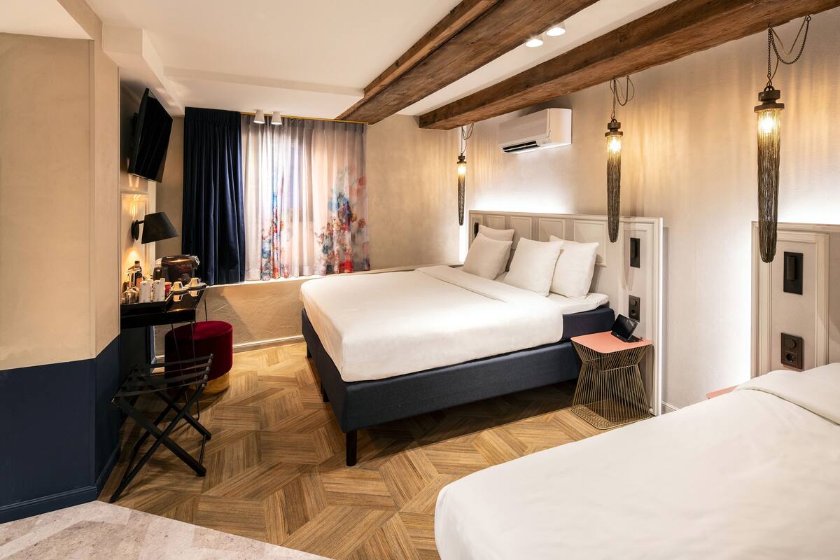 Una habitación de hotel con una cama grande, un escritorio con silla, una mesita pequeña y un televisor montado en la pared.