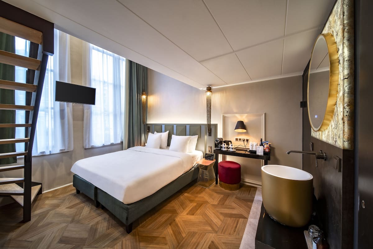 Habitación de hotel con una cama grande, un escritorio con silla, una tocador con espejo y una bañera amplia, además de piso de madera.
