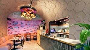 Un restaurante con un mural colorido, una zona de bar y diferentes disposiciones de mesas.