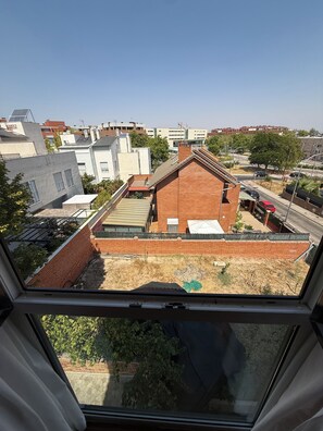 A residential area with a mix of modern and traditional buildings, a clear sky, and a view through a window. - Hostal Los Coronales (Madrid)