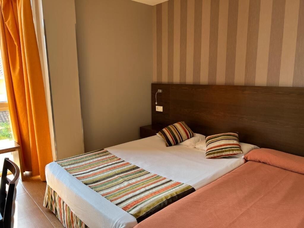 A hotel room with a bed, a wooden headboard, and a window with curtains.