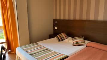 A hotel room with a bed, a wooden headboard, and a window with curtains.