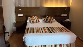 Una habitación de hotel con una cama grande, un cabecero de madera, una mesita de noche con un teléfono y una lámpara fijada a la pared.