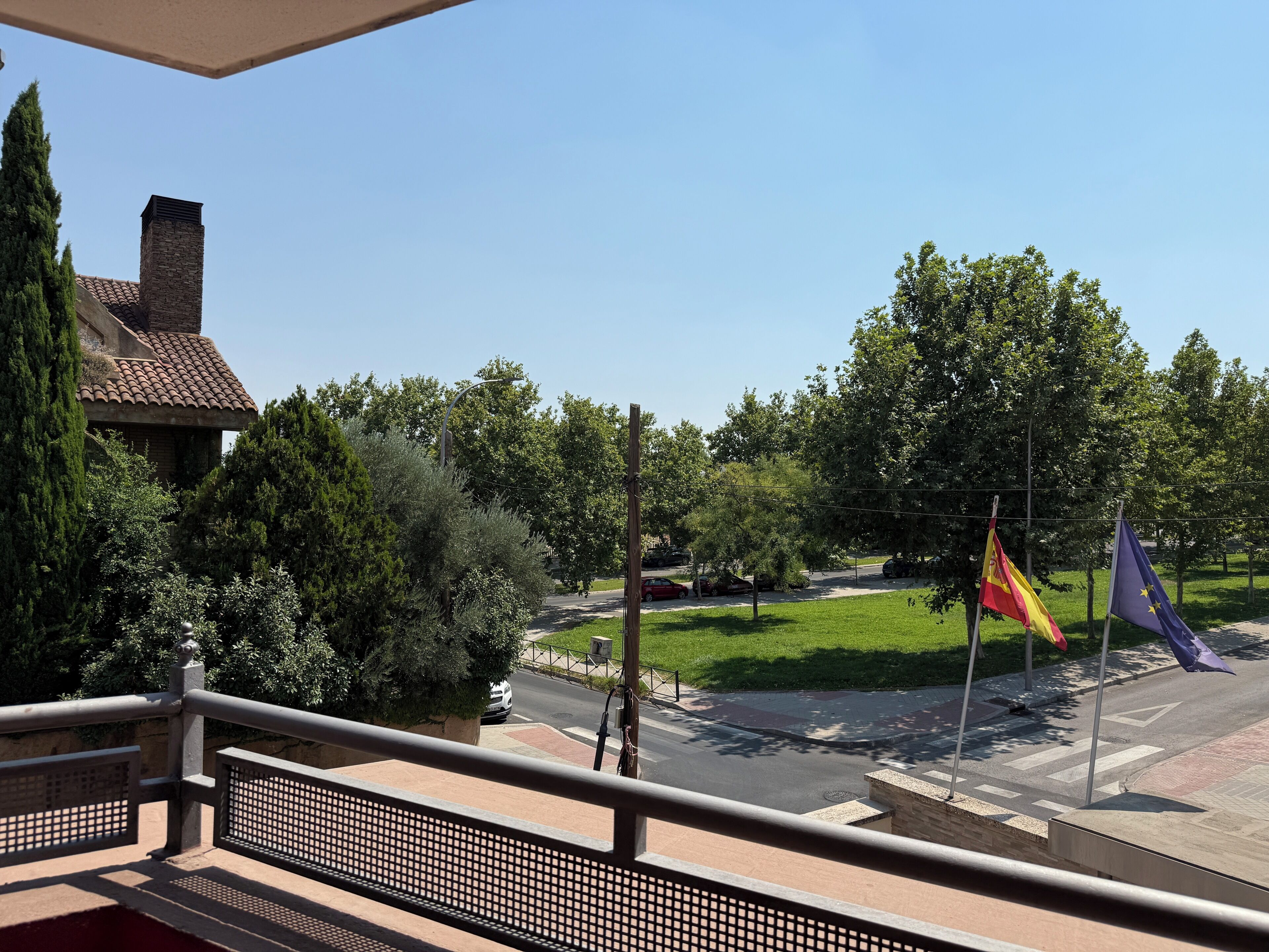 A balcony with a view of a street, trees, and flags.