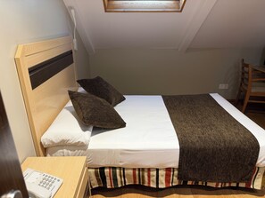 A single bed with a headboard, two pillows, a white bedspread, a striped blanket, and a wooden nightstand with a telephone. - Hostal Los Coronales (Madrid)