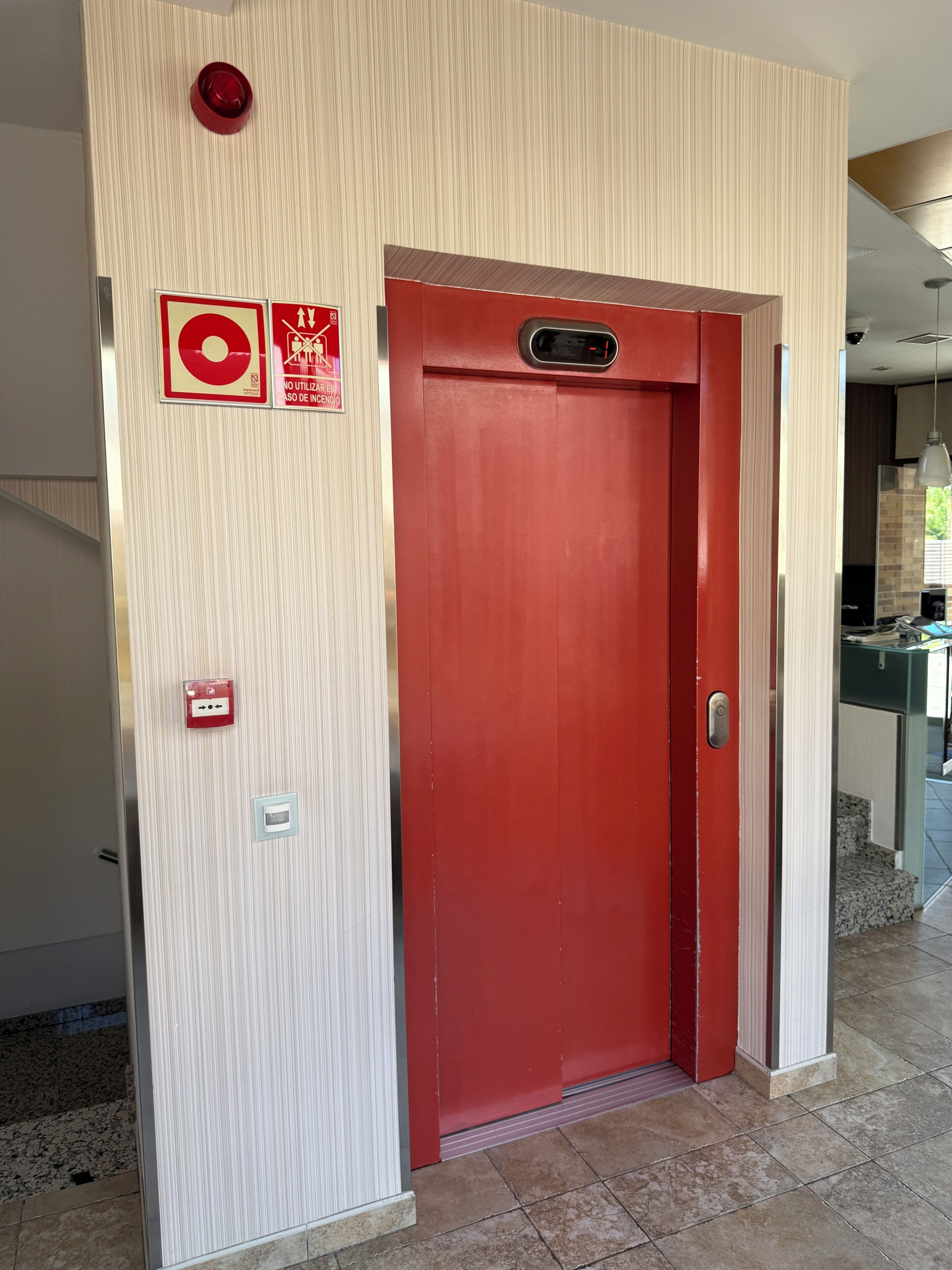 A red door with a fire alarm and emergency exit sign on the wall.