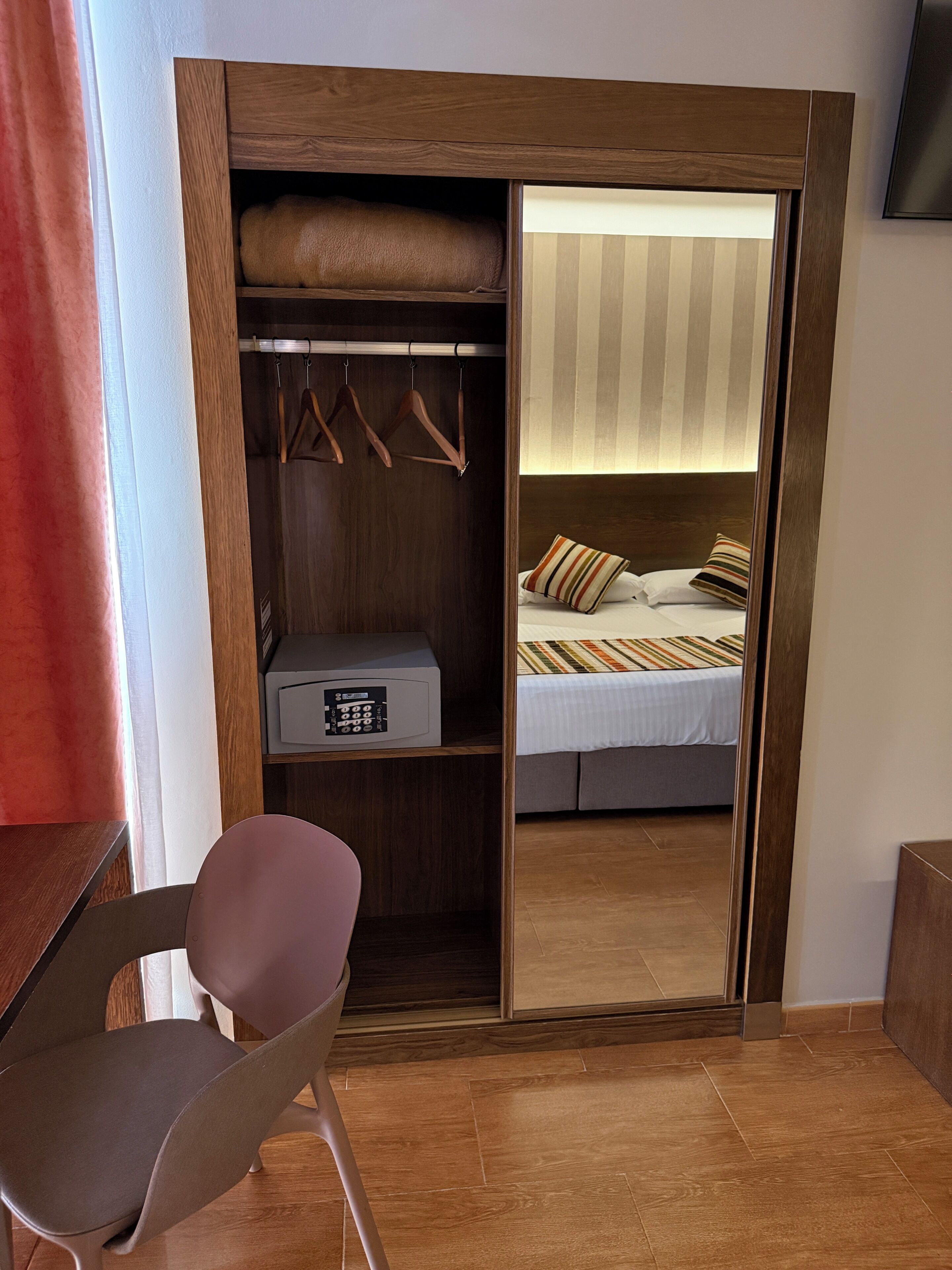 A bedroom with a bed, a wardrobe, a chair, and a bedside table.