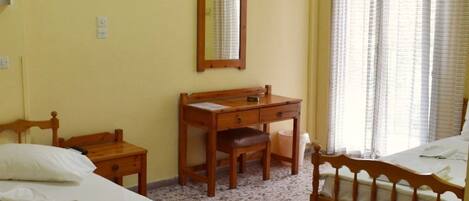 A room with two wooden beds, a wooden desk, a chair, a mirror, and an air conditioning unit.
