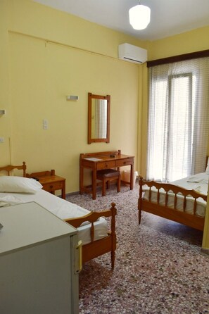 A room with two wooden beds, a wooden desk, a chair, a mirror, and an air conditioning unit. - Asteria (Zakynthos)