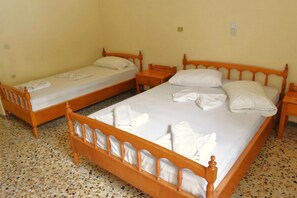 A room with two wooden beds, each with white linens and pillows, and a small wooden nightstand between them.