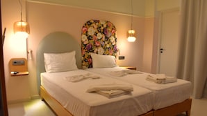Een tweepersoonsbed met witte lakens, een bloemen hoofdbord, bedlampjes en een deur.