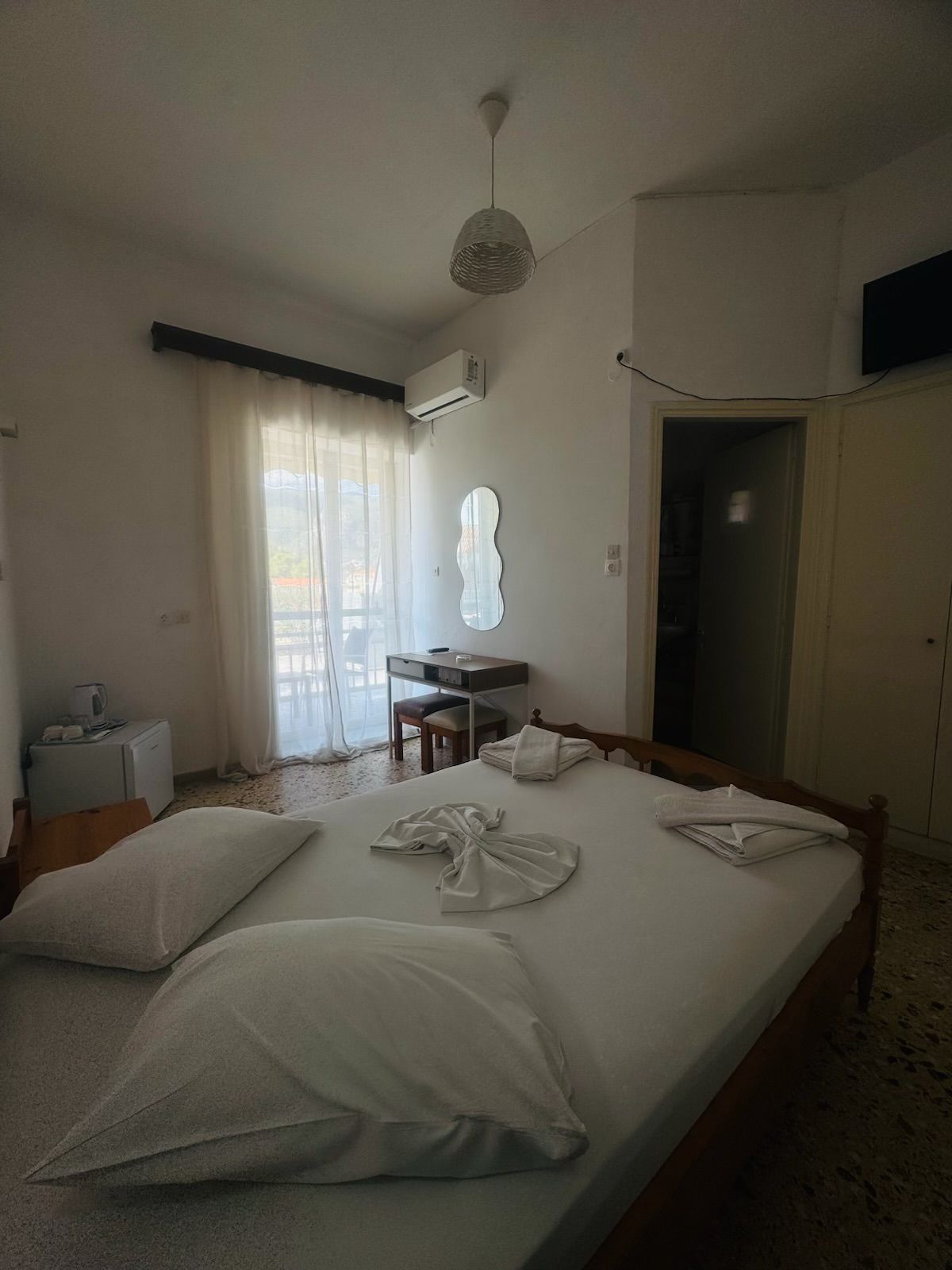 Une chambre d’hôtel équipée d’un lit, d’un bureau, d’une chaise, d’un climatiseur et d’un téléviseur fixé au mur.