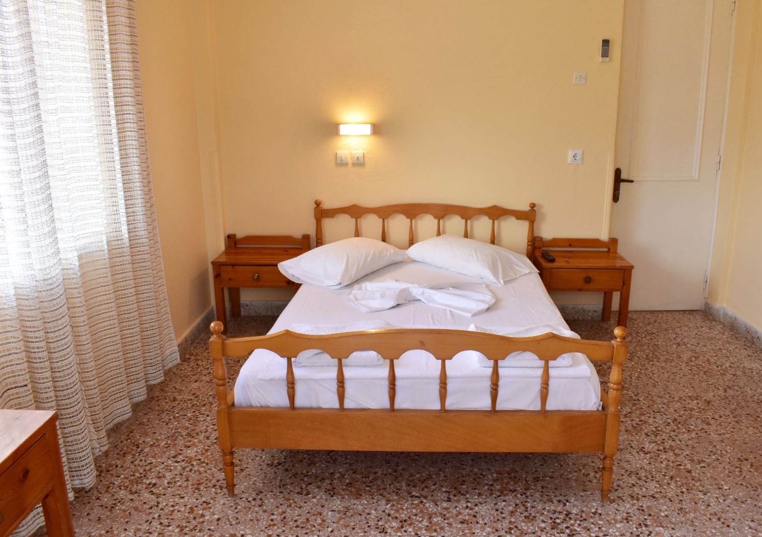A single bed with a wooden frame, two bedside tables, a wall-mounted light, and a door.
