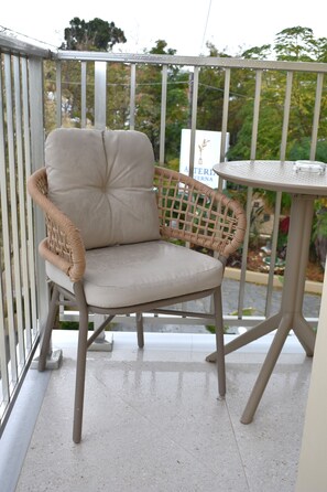A wicker chair with a cushioned seat and backrest, positioned on a balcony with a metal railing. - Asteria (Zakynthos)