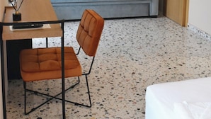Een kamer met een bank, een bureau met stoel, een bed, een hanglamp en een airconditioning.