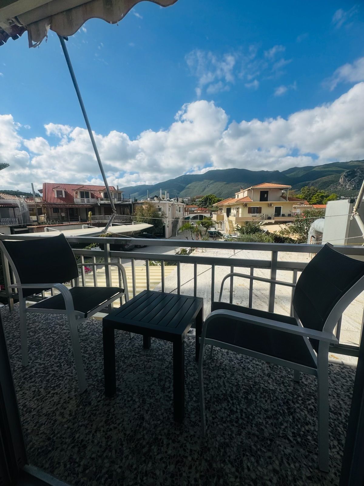 A terrace with a table and chairs, overlooking a town with buildings and mountains in the background.