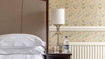 A neatly made bed with white linens, a bedside table with a lamp, and a wall with a floral pattern.