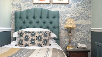 A neatly made bed with patterned pillows, a tufted headboard, and a bedside table with a lamp and a telephone.