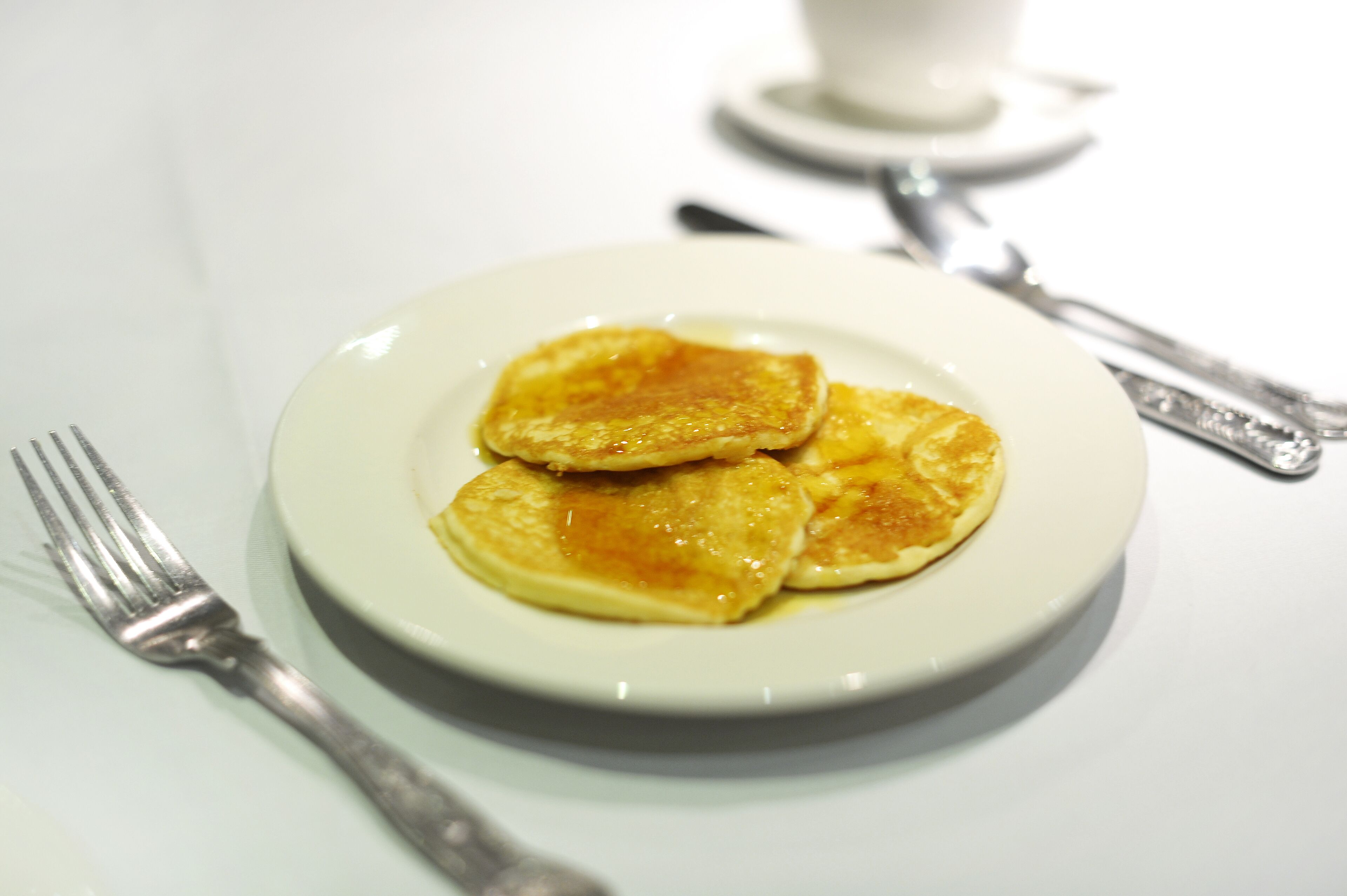 A plate of pancakes with syrup, accompanied by a fork and a knife on a white table.