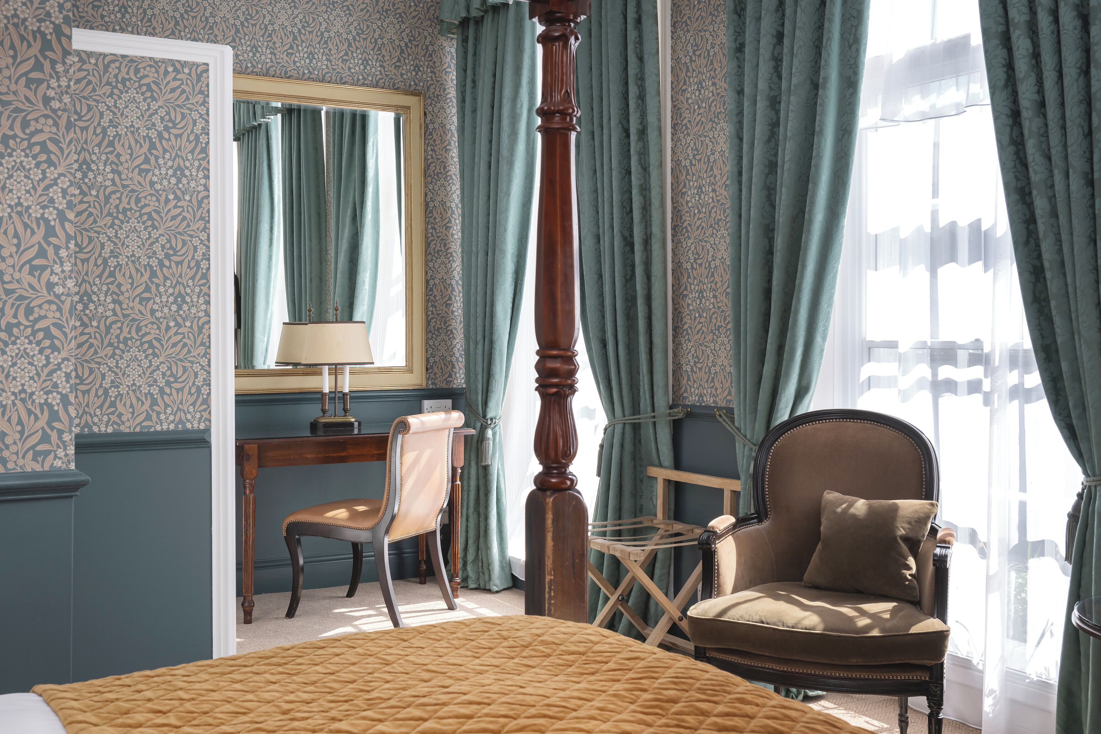 A bedroom with a bed, a chair, a desk, and a mirror.