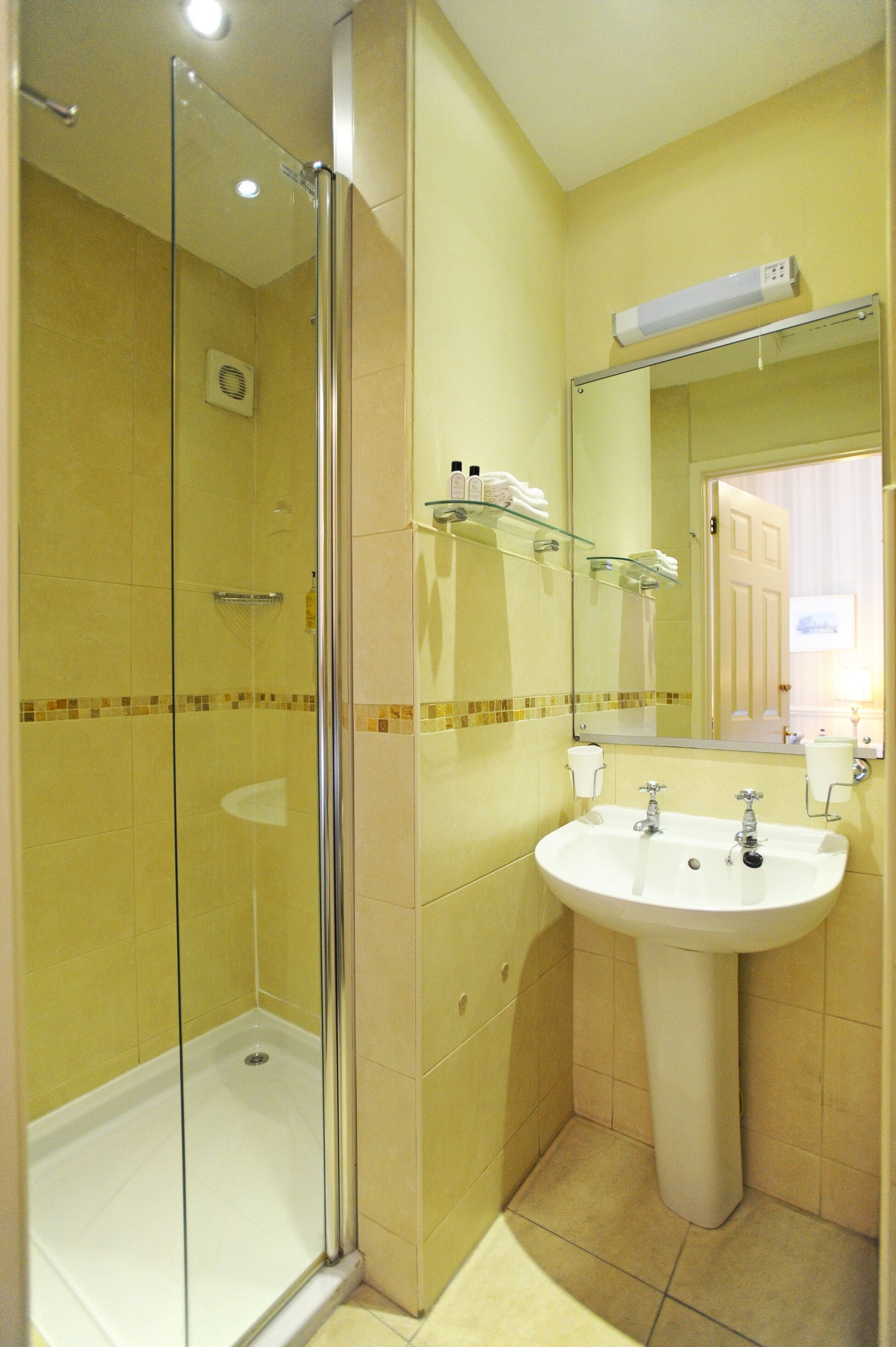 A bathroom with a glass-enclosed shower, a pedestal sink, and a mirror above the sink.