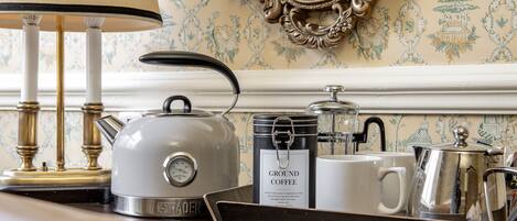 A vintage-style kitchen with a white kettle, a coffee pot, a tray with a coffee can, and a white mug.