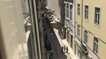 Ruas estreitas com edifícios em ambos os lados, uma carrinha branca estacionada na berma e alguns pedestres a caminhar.